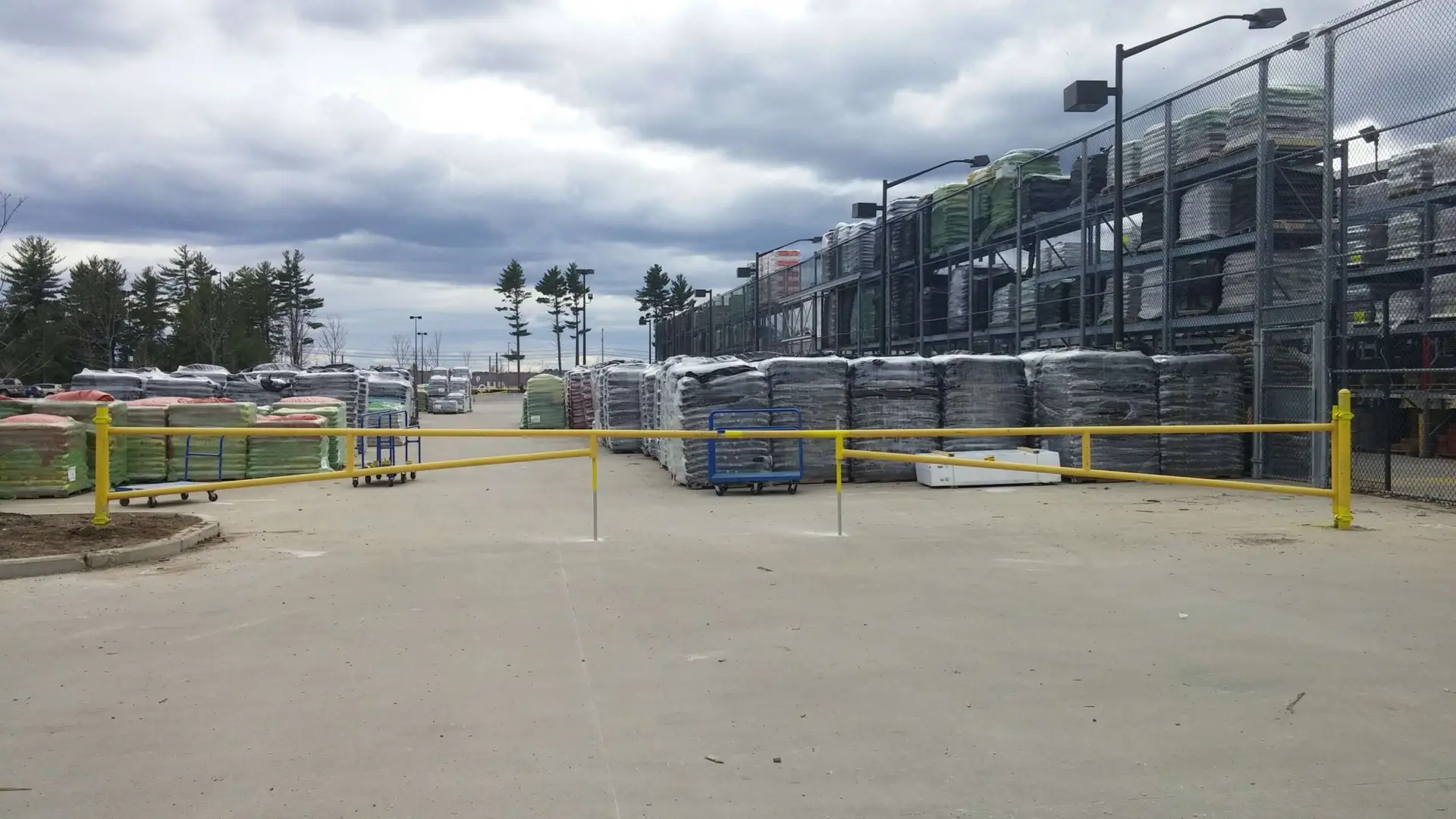 Olympic Fence Co. yard in West Newbury with chain-link fencing and stacked materials, showcasing quality fencing products and a lifetime workmanship warranty.