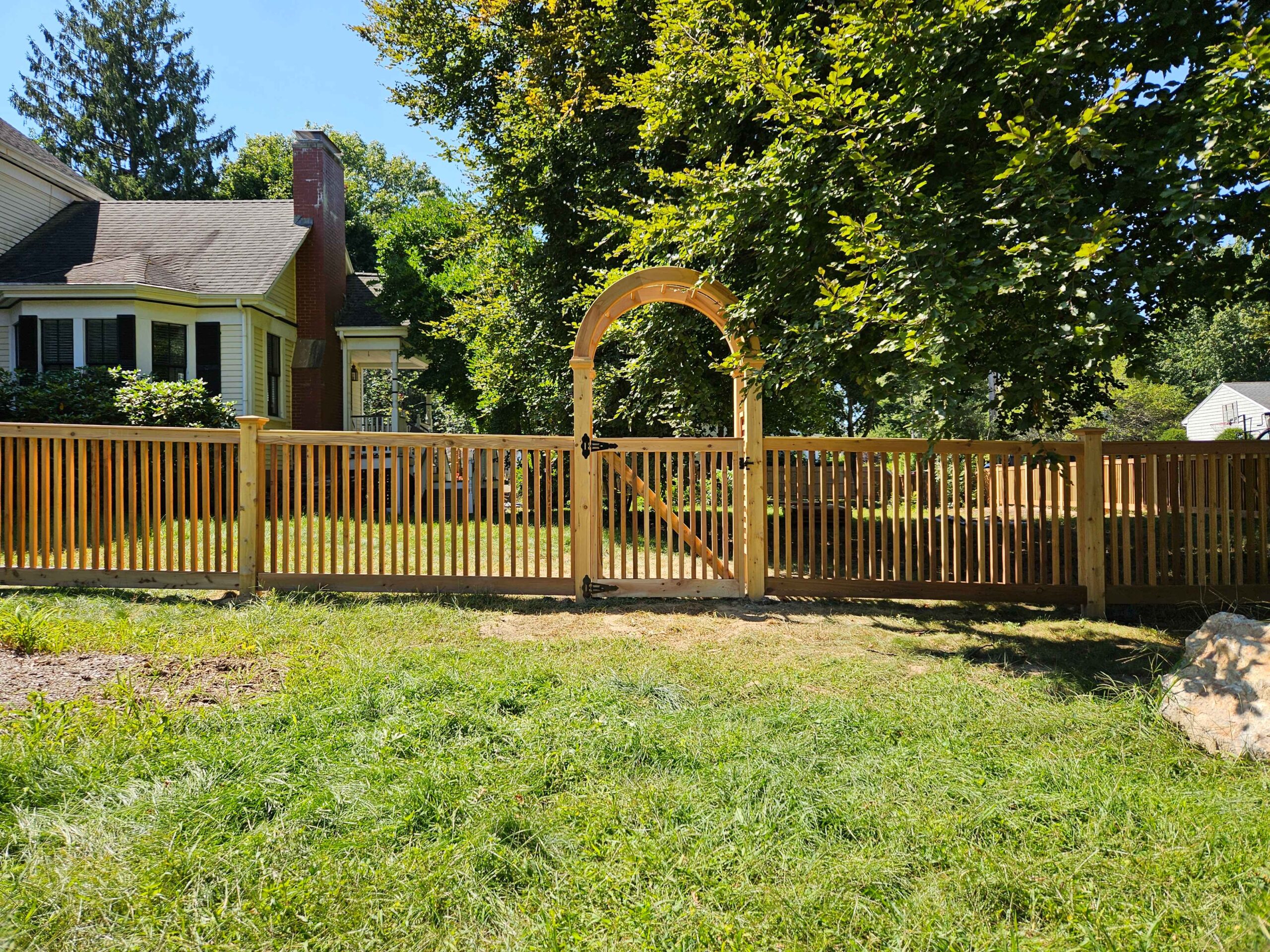 Cedar fence installation featuring a decorative archway gate, showcasing the natural beauty and durability of Western Red Cedar in a residential setting.