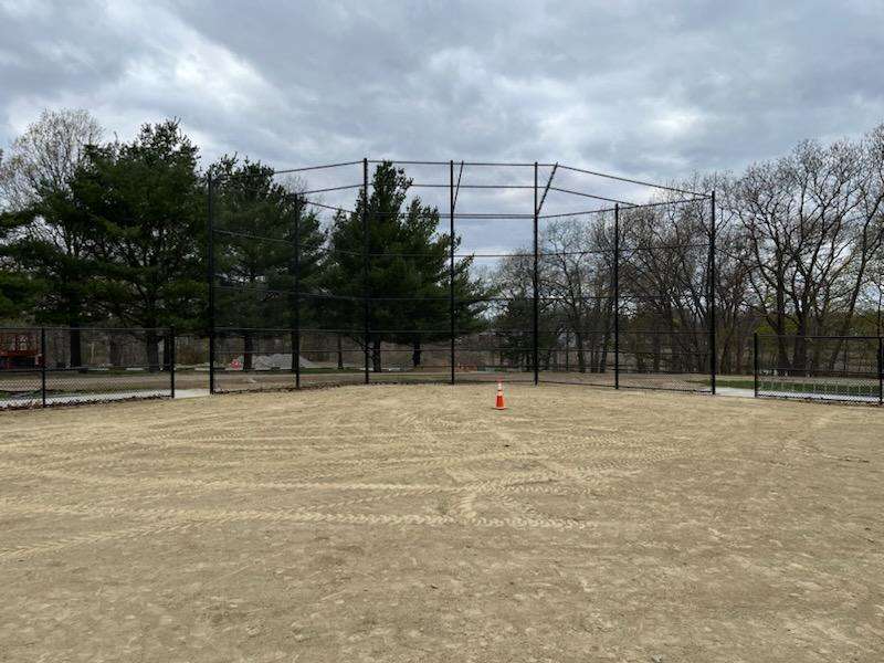 Baseball backstop and chain link fencing installed at a sports facility in Amesbury, MA, surrounded by a sandy field and trees.