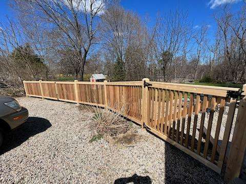 Cedar wood fencing installation showcasing classic New England aesthetics, featuring a durable wood-on-steel system in a residential setting, with a gravel pathway and trees in the background.