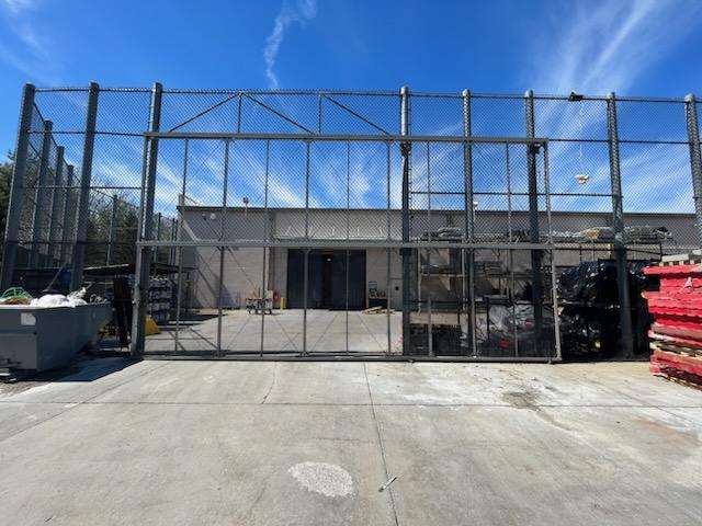 Chain-link security fence enclosing a commercial property with a large gate, surrounded by storage equipment and a clear blue sky.