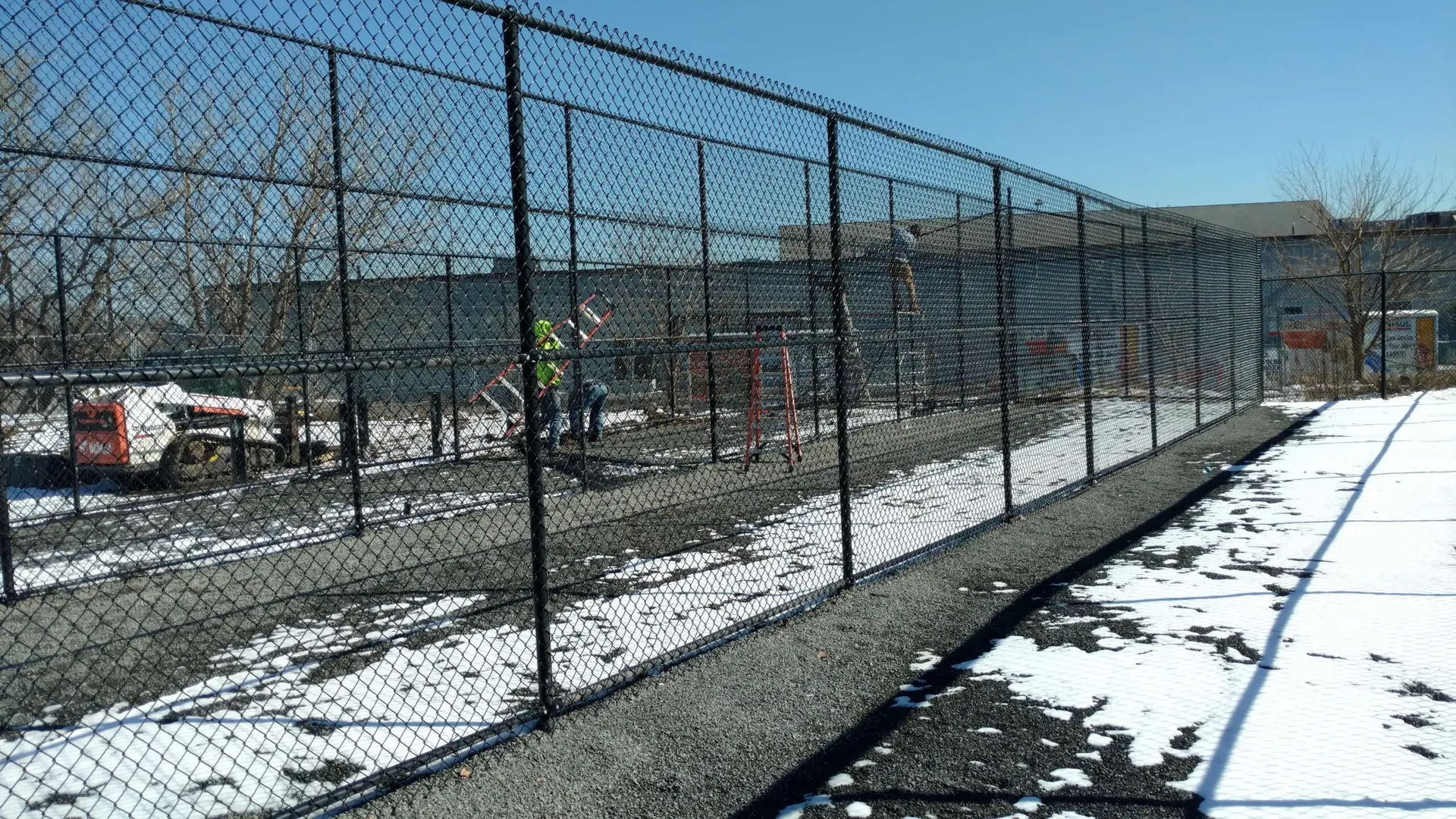 Chain link fence installation in progress, featuring workers and equipment, surrounded by snow and gravel, illustrating Olympic Fence Co.'s commercial fencing services in Salisbury, MA.