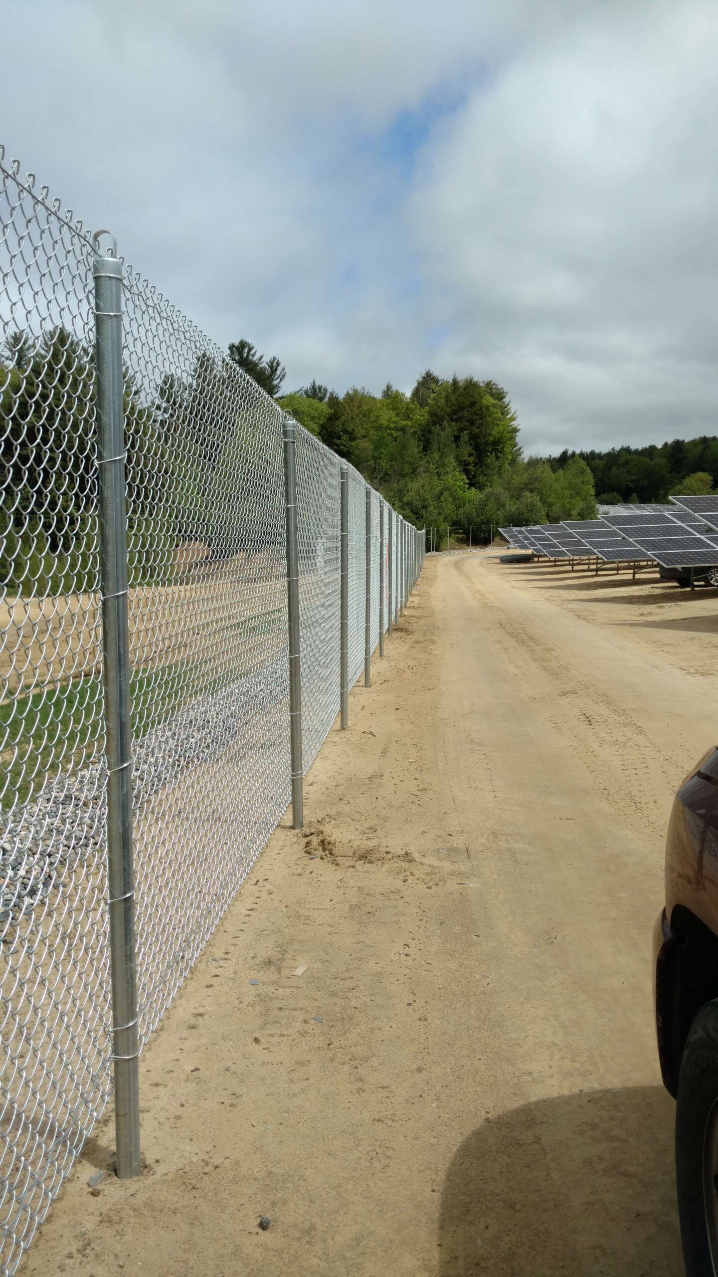 Chain-link fencing along a dirt path near solar panels, illustrating durable security solutions for commercial properties in North Andover.