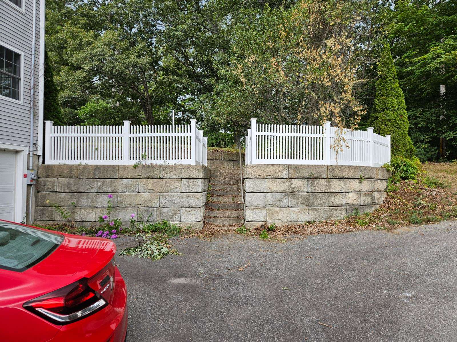 White vinyl fence with decorative pickets surrounding a raised stone wall, featuring a staircase and greenery in a residential setting in Salisbury.