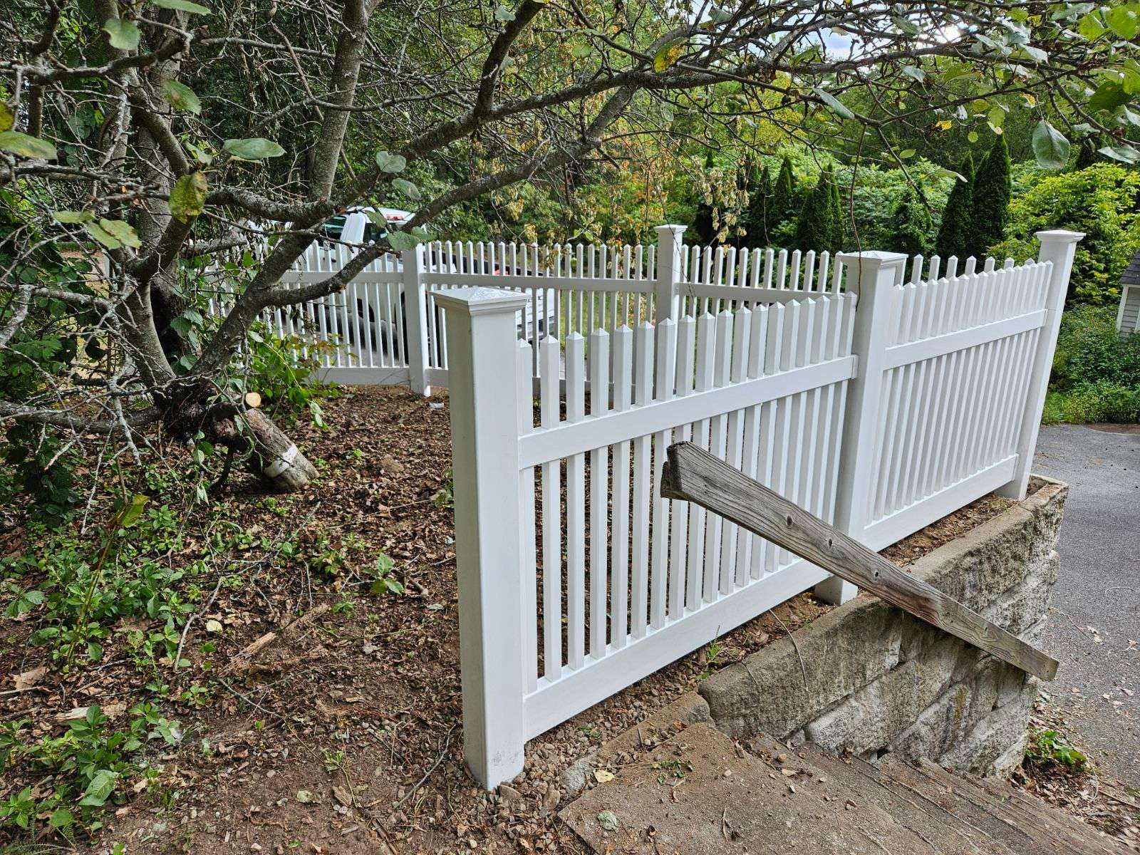 Vinyl picket fence surrounding a landscaped area, showcasing classic design and maintenance-free white finish, ideal for Merrimac homes and enhancing curb appeal.