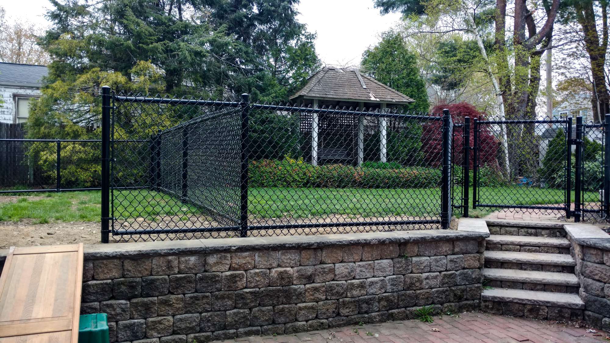 Chain link fence enclosing a grassy yard with a gazebo, featuring a stone wall and steps, illustrating residential fencing options for Salisbury homeowners.
