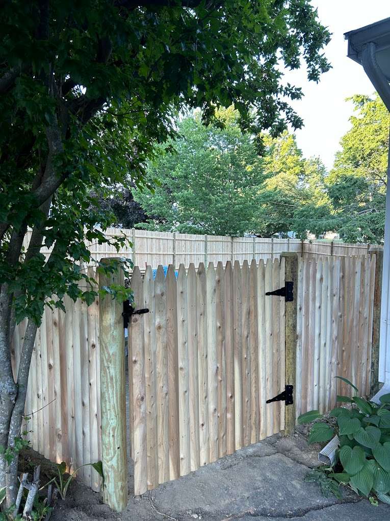Cedar fence gate with sturdy black hinges, surrounded by greenery, showcasing quality craftsmanship and natural beauty in a residential setting.