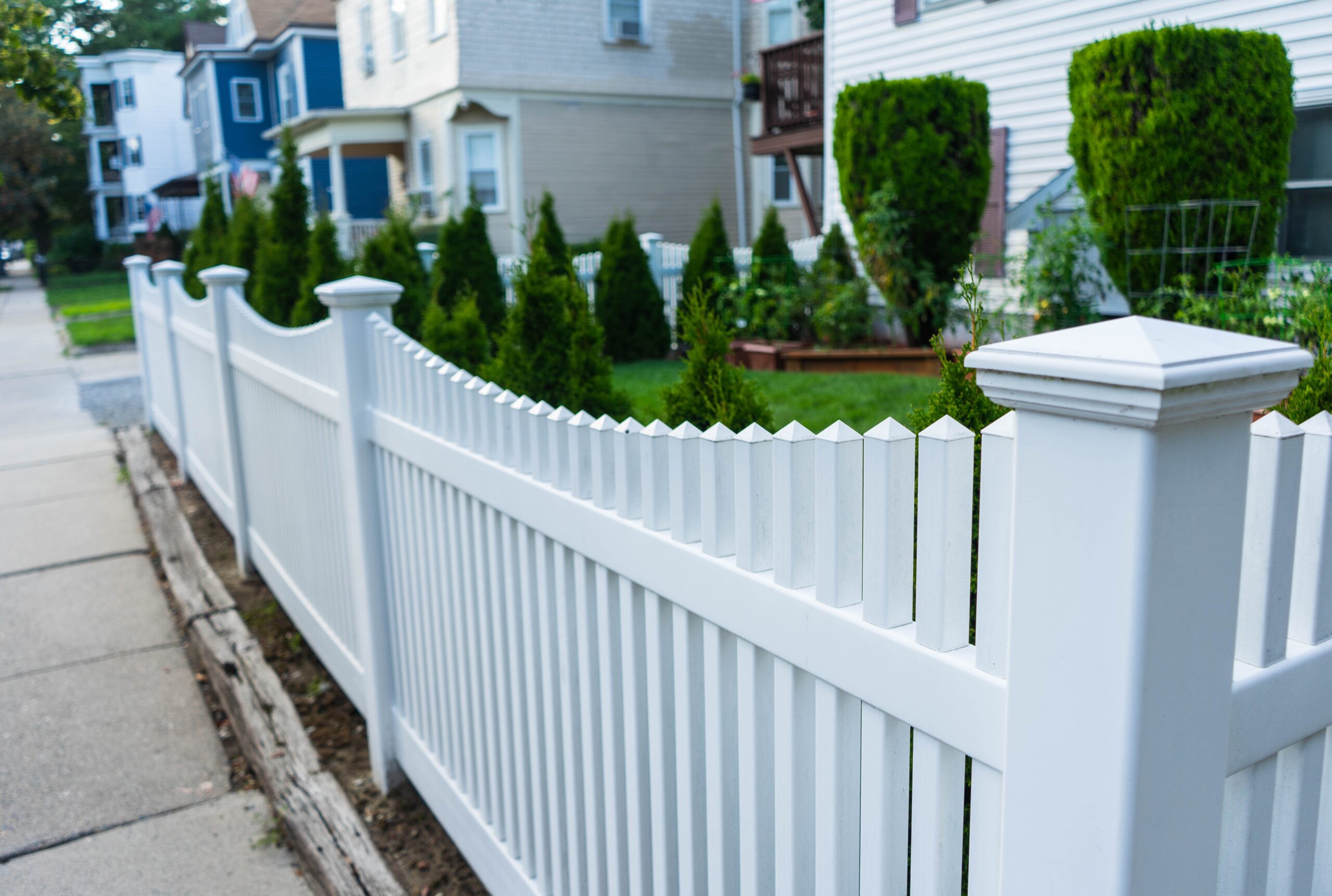 White picket fence in a residential neighborhood in Amesbury, MA, showcasing Olympic Fence Company’s vinyl fence styles.