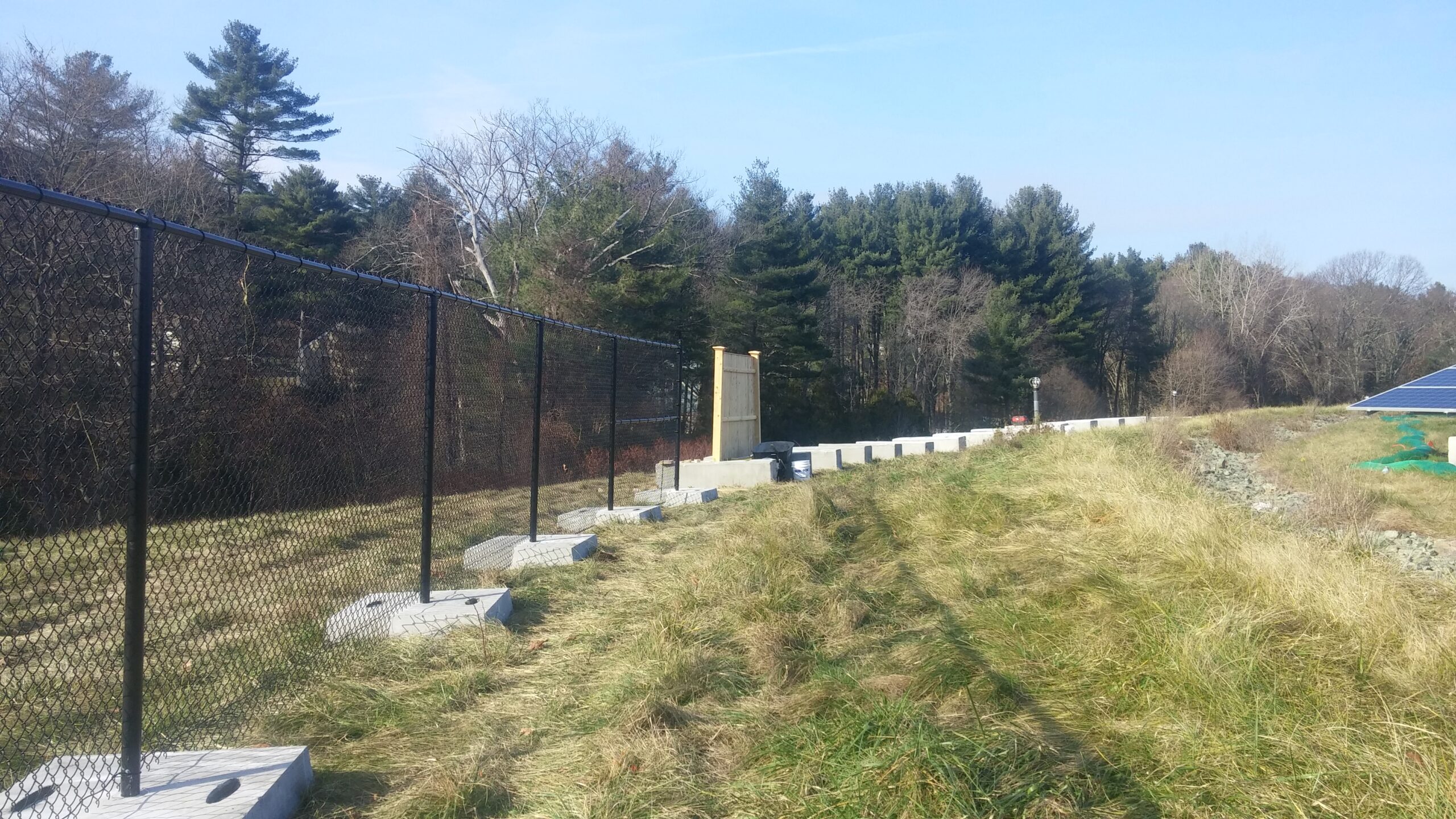 Black vinyl-coated chain link fence installed by Olympic Fence Co. in West Newbury, Massachusetts.