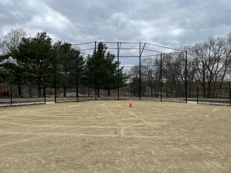 Chain link fence installation in a sandy area, surrounded by trees, with a construction cone in the center, showcasing the fencing options available for Newburyport properties.