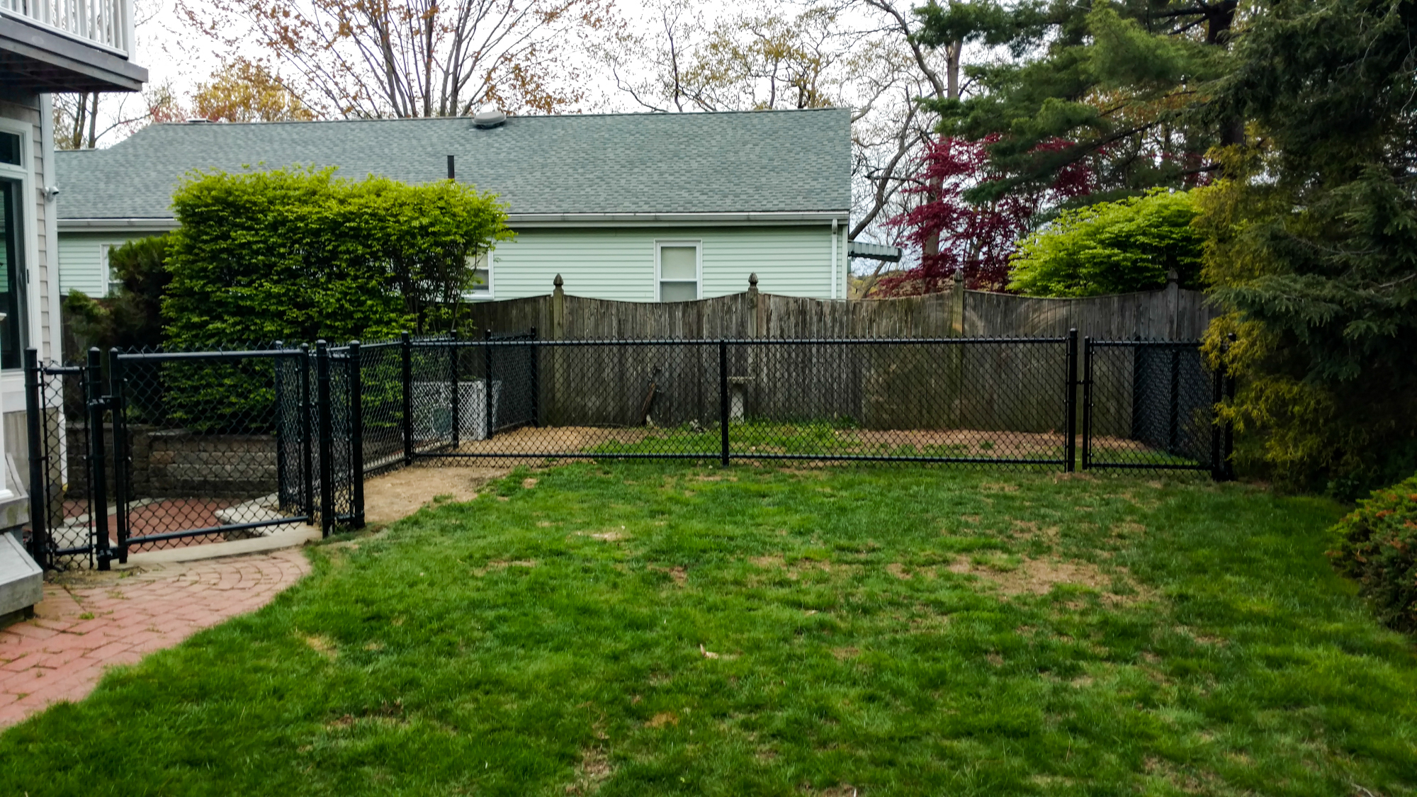 Residential chain link fence installation in Newburyport, featuring a black fence enclosing a backyard with green grass and surrounding foliage.