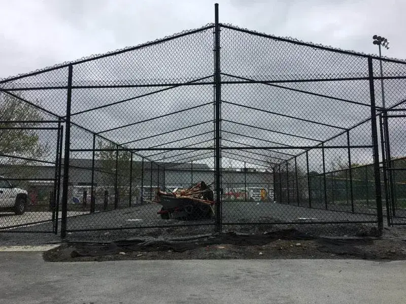 Chain link fence installation in a sports facility, showcasing a secure enclosure with a gravel surface and construction materials visible, emphasizing durability and safety for athletic activities.
